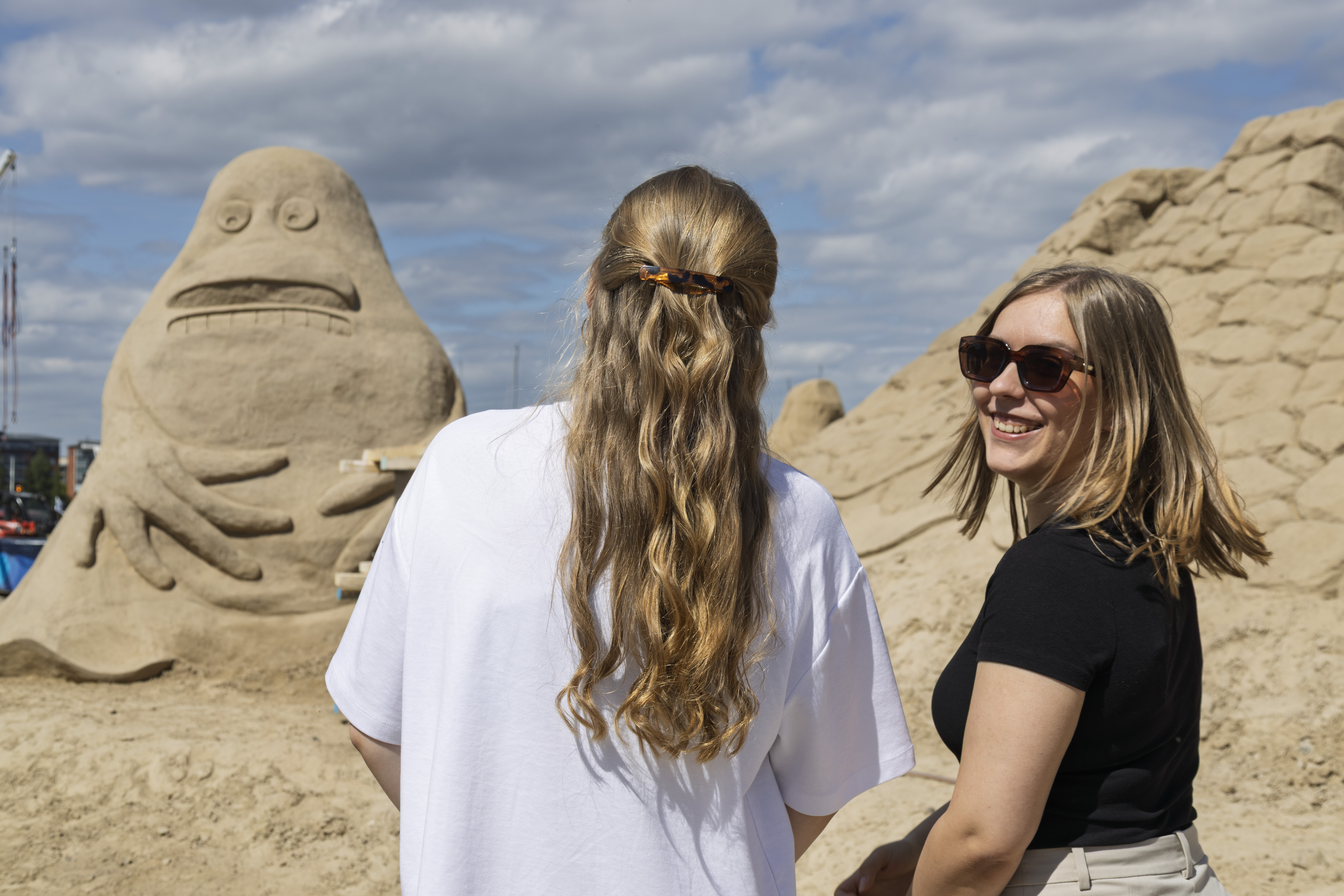 Two women stand in front of a sand sculpture depicting The Groke
